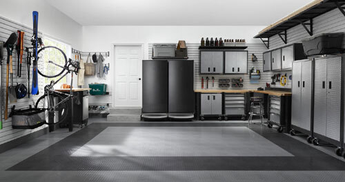 Complete garage organization system with tall modular cabinets, a workbench, overhead racks, and a garage-ready refrigerator.
